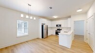 Located at 5171 Bowman Rd in Macon, GA, this well-designed single-story home offers a clean, modern aesthetic throughout. Light hardwood flooring runs continuously across the main living areas, creating a cohesive and bright interior. The open-concept kitchen and living room form the heart of the home, maximizing usable space and encouraging an easy flow between areas. The kitchen is outfitted with crisp white shaker cabinets — both upper and lower — paired with light countertops, a peninsula with sink, and a full suite of stainless steel appliances including a refrigerator, range, microwave, and dishwasher. A stylish pendant chandelier anchors the dining area, while a window allows natural light to fill the space. The bedroom is a comfortable, well-proportioned retreat featuring a ceiling fan, a window with natural light, and access to a dedicated closet. The bathroom includes a vanity with a white countertop sink, ample cabinet storage, and continued hardwood-style flooring. Additional functional spaces include a laundry area and utility room. The attached garage features an automatic door opener and direct interior access, adding everyday convenience to this tidy, move-in-ready home.