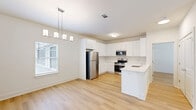 Located at 5171 Bowman Rd in Macon, GA, this well-designed single-story home offers a clean, modern aesthetic throughout. Light hardwood flooring runs continuously across the main living areas, creating a cohesive and bright interior. The open-concept kitchen and living room form the heart of the home, maximizing usable space and encouraging an easy flow between areas. The kitchen is outfitted with crisp white shaker cabinets — both upper and lower — paired with light countertops, a peninsula with sink, and a full suite of stainless steel appliances including a refrigerator, range, microwave, and dishwasher. A stylish pendant chandelier anchors the dining area, while a window allows natural light to fill the space. The bedroom is a comfortable, well-proportioned retreat featuring a ceiling fan, a window with natural light, and access to a dedicated closet. The bathroom includes a vanity with a white countertop sink, ample cabinet storage, and continued hardwood-style flooring. Additional functional spaces include a laundry area and utility room. The attached garage features an automatic door opener and direct interior access, adding everyday convenience to this tidy, move-in-ready home.
