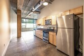 This single-floor loft-style unit showcases a distinctive urban industrial aesthetic throughout its well-organized layout. Exposed concrete ceilings with visible ductwork and structural concrete columns create a raw, warehouse-inspired character, while large-format tile and polished concrete flooring provide a clean, durable foundation underfoot. Pendant lighting adds warm accents against the industrial backdrop.

The open living area benefits from natural light streaming through large windows that frame outdoor greenery, lending an airy quality to the space. The galley-style kitchen is thoughtfully equipped with light maple cabinetry, dark granite countertops, stainless steel appliances including a gas range, microwave, dishwasher, and refrigerator — offering full functionality within a compact footprint.

The bathroom features a tiled tub-and-shower combination with striking dark slate wall tile, a light wood vanity with a dark countertop and stainless steel vessel sink, and a wall-mounted sconce, creating a modern, polished look. An in-unit washer and dryer area adds practical convenience. The overall ambiance of the unit blends industrial rawness with clean, modern finishes, making it a distinctive and functional urban living space.
