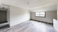 Located at 96 Ledgecrest Ave in New Britain, CT, this single-floor residence offers three bedrooms, one bathroom, and a hallway, all thoughtfully arranged within a compact yet functional layout. The unit is finished with light gray luxury vinyl plank flooring that runs consistently throughout, complementing the neutral, soft gray wall tones and textured popcorn ceilings found in every room.

The spacious primary bedroom benefits from vaulted ceilings that enhance the sense of openness, along with a wall-mounted light fixture and its own private entry door. Additional bedrooms feature similar vaulted or angled ceiling lines, natural light from exterior-facing windows with views of the surrounding neighborhood, and ample closet space — one bedroom includes a built-in double-door closet.

The bathroom is clean and bright, finished with white subway-style wall tiles surrounding a tub-shower combination, a single vanity with mirror, and a window that brings in natural light. A dedicated hallway connects the rooms, while a glimpse of cabinetry in warm wood tones suggests a kitchen area with functional storage. Overall, the space presents a fresh, move-in-ready aesthetic with consistent finishes throughout.