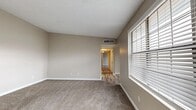 This single-floor residence offers a practical and comfortable layout designed for everyday living. The main living area features plush carpeting, neutral beige walls, a textured ceiling, and a large window fitted with horizontal blinds that invites natural light into the space. A central HVAC vent ensures year-round climate control. The flooring transitions to wood-look vinyl planks in the hallways and wet areas, providing a clean, cohesive aesthetic throughout.

The bedrooms are carpeted and well-sized, each featuring ceiling fans with integrated lighting, windows with blinds, and generous closet space—including a mirrored sliding-door closet and a walk-in closet with built-in shelving. The bathrooms are finished with wide vanity countertops, dark wood cabinetry, large mirrors, and light tile flooring. One bathroom includes a full soaking tub, while another features a dedicated shower area.

The kitchen is outfitted with dark wood cabinetry, light countertops, a double-basin stainless steel sink, and a dishwasher, offering efficient functionality. A dedicated walk-in laundry or storage closet with hanging rods adds convenience. The overall palette of warm neutrals and clean white trim creates a bright, welcoming ambiance throughout the home.