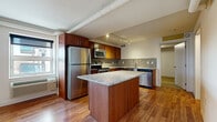 This thoughtfully designed one-bedroom, one-bathroom unit offers a comfortable and functional layout across a single floor. The open-concept kitchen is a standout feature, showcasing rich warm-toned cabinetry, granite countertops, and a mosaic tile backsplash. A large central island with matching granite provides additional workspace and storage. Stainless steel appliances, including a refrigerator, range, microwave, and dishwasher, complete the well-equipped kitchen. Track lighting illuminates the space, complementing the warm hardwood floors that extend throughout the main living areas. The living room is bright and airy, featuring exposed ductwork that adds an industrial touch, along with a glass door offering access to an outdoor area and allowing natural light to fill the room. The bedroom is carpeted for comfort and is served by a dedicated walk-in closet equipped with wire shelving for organized storage. The bathroom features neutral tile flooring, a warm wood vanity with granite countertop, and clean white walls. A hallway connects the rooms, contributing to an efficient and practical overall flow.