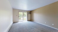 This single-floor, 2-bedroom, 1-bathroom residence at 1447 Woodview Dr in Schererville, Indiana offers a practical and well-organized layout. The living room is a comfortable, carpeted space featuring a sliding glass door that fills the room with natural light and provides views of the surrounding greenery. A wall-mounted air conditioning unit serves the living area, and a baseboard heating system is present throughout the unit.

The kitchen is equipped with warm-toned wood cabinetry, light laminate countertops, a stainless steel sink, tile flooring, and a dishwasher, offering functional storage and workspace. The layout connects the kitchen conveniently to the living area.

Both bedrooms are carpeted and receive natural light through windows that overlook lush outdoor foliage. Each bedroom includes closet storage, and one features a spacious walk-in closet with wire shelving and hanging rods. Wall-mounted air conditioning and baseboard heating units are also present in the bedrooms.

The bathroom includes a tiled tub-shower combination, a wood-cabinet vanity with a light countertop, and tile flooring. A hallway connects the main living spaces, completing the efficient and cohesive floor plan.