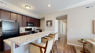Located at 1564 McNaughten Rd in Columbus, Ohio, this single-floor residence offers a well-designed layout with a cohesive neutral color palette and thoughtful finishes throughout. The open-concept kitchen is a standout feature, showcasing rich dark mahogany cabinetry, light granite countertops, and black appliances including a refrigerator, range, and over-the-range microwave. A spacious kitchen island with a built-in sink and seating for two serves as the centerpiece, seamlessly connecting the kitchen to the living and dining areas. The living room is bright and airy, with soft carpeting, large windows allowing natural light to filter in, and access to additional areas of the unit. The primary bedroom offers plush carpeting, a window with exterior views, and a calm, restful atmosphere. A secondary bedroom provides comfortable accommodations with neutral walls and soft carpet flooring. The bathrooms are finished with tile flooring, dark wood vanities topped with granite counters, large mirrors, and well-lit fixtures. Hardwood-style flooring flows through the kitchen and main corridors, adding warmth and continuity. The overall ambiance is clean, modern, and inviting, making this a functional and comfortable living space.