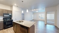 Located at 355 N Mill Rd in Vineyard, Utah, this single-floor residence offers a thoughtfully designed layout with modern finishes throughout. The open-concept kitchen serves as the heart of the home, featuring rich dark wood cabinetry, granite-look countertops, a central island with a double stainless steel sink, pendant lighting, and black appliances including a refrigerator, range, and dishwasher. Light wood-style flooring extends seamlessly through the kitchen and into the living area, creating a cohesive flow. The living space is bright and airy, with natural light streaming in through large windows fitted with blinds, and a sliding glass door providing additional light and outdoor access. Bedrooms are carpeted for comfort and offer windows with views of the surrounding neighborhood. The bathrooms are cleanly appointed with wood-toned vanities topped with granite-look counters, large mirrors, wood-style tile flooring, and tub-shower combinations. A programmable thermostat and ample storage space contribute to everyday functionality. The overall aesthetic is contemporary and neutral, with white walls and clean lines that create a fresh, move-in-ready environment well-suited to a variety of lifestyles.