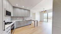 This well-appointed 2-bedroom, 2-bathroom residence is thoughtfully designed with modern finishes and an efficient, functional layout across a single floor. The open-concept kitchen anchors the living area and features sleek gray shaker-style cabinetry, a tiled backsplash, white countertops, and an integrated peninsula that doubles as a dining surface. A stylish multi-arm pendant chandelier adds a contemporary touch, while a glass door opens directly onto a private balcony offering open outdoor views. Light hardwood flooring runs seamlessly throughout the entire unit, lending warmth and visual continuity. A stacked in-unit washer and dryer is conveniently situated adjacent to the kitchen. The bedrooms are bright and well-proportioned, with large windows framing scenic outdoor views and crown molding adding an elegant architectural detail. The primary bedroom features its own balcony access via a classic paneled door. Both bathrooms are finished to a high standard, showcasing marble-look wall tiles, intricate patterned floor tiles, a wall-mounted toilet, undermount sink with stone countertop, and a frameless glass-enclosed shower — creating a clean, spa-like atmosphere. A hallway connects the living and private areas, completing this refined and move-in-ready residence.
