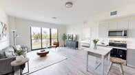 Located in Oakland Park, Florida, this well-appointed 2-bedroom, 2-bathroom residence offers a clean, contemporary design with an open and airy feel throughout. Light wood-style flooring runs continuously across the single-level floor plan, tying the spaces together seamlessly.

The open-concept living and kitchen area serves as the heart of the home. The living room is bathed in natural light from large floor-to-ceiling sliding glass doors that frame lush palm tree views, creating an effortless indoor-outdoor connection. The kitchen features flat-front gray cabinetry extending to the ceiling, stainless steel appliances, a clean white countertop, and a compact dining table—thoughtfully designed for both function and style.

Both bedrooms are generously proportioned, with the primary bedroom offering its own large sliding glass door with palm-lined views and direct access to natural light. Each bedroom is served by a dedicated closet, including a walk-in closet equipped with wire shelving systems that maximize storage. The two bathrooms mirror the home's clean aesthetic, featuring white subway tile walk-in showers with chrome fixtures and light tile flooring.

A hallway connects the private and shared areas of the home, contributing to a practical and well-organized layout. The consistently neutral palette, abundant natural light, and modern finishes give this residence a bright, welcoming ambiance throughout.