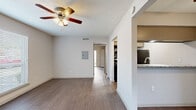 This efficiently designed one-bedroom, one-bathroom unit offers a well-organized single-floor layout that maximizes every square foot. Hardwood-style flooring runs throughout the living areas and bedroom, providing a cohesive and low-maintenance aesthetic. Ceiling fans are installed in every room, ensuring consistent airflow and comfort.

The living room receives natural light through a large window fitted with horizontal blinds, creating a bright and open atmosphere. It connects seamlessly to the kitchen via a peninsula-style pass-through counter topped with granite, making the space feel open and functional. The galley kitchen is well-appointed, featuring granite countertops, a tile backsplash, cream cabinetry, black appliances including a range, microwave, and refrigerator, and a stainless steel sink.

The bedroom is a comfortable size, offering a ceiling fan, a window with outdoor views, a sliding glass door leading to a private patio, and access to a closet with built-in shelving. A second closet provides additional storage. The bathroom includes a full tub-shower combination with large white tile surround, complemented by granite vanity counters and wood-look flooring.