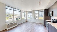 Located at 3750 S River Pkwy in Portland, Oregon, this thoughtfully designed single-floor unit offers a clean, contemporary aesthetic throughout. The open-concept kitchen and living room serves as the heart of the space, where floor-to-ceiling windows flood the area with natural light and frame sweeping views of the surrounding Portland cityscape and tree-lined hillsides. The kitchen is outfitted with stainless steel appliances, including a refrigerator, electric range, and built-in microwave, complemented by dark wood-grain cabinetry, white countertops, and a subway tile backsplash. Hardwood-style flooring runs through the main living areas, adding warmth and continuity. The bedrooms feature plush carpeting and large windows that continue the urban views, with one room boasting a wide sliding-door closet for generous storage. Three closets in total provide ample organizational space throughout. The primary bathroom features rich dark wood cabinetry, a built-in vanity with a white countertop, and warm wood-tone flooring, while the combined bathroom and laundry offers added convenience. Recessed lighting and a neutral color palette create a bright, cohesive ambiance throughout this well-appointed Portland residence.
