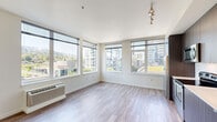 Located at 3750 S River Pkwy in Portland, Oregon, this thoughtfully designed single-floor unit offers a clean, contemporary aesthetic throughout. The open-concept kitchen and living room serves as the heart of the space, where floor-to-ceiling windows flood the area with natural light and frame sweeping views of the surrounding Portland cityscape and tree-lined hillsides. The kitchen is outfitted with stainless steel appliances, including a refrigerator, electric range, and built-in microwave, complemented by dark wood-grain cabinetry, white countertops, and a subway tile backsplash. Hardwood-style flooring runs through the main living areas, adding warmth and continuity. The bedrooms feature plush carpeting and large windows that continue the urban views, with one room boasting a wide sliding-door closet for generous storage. Three closets in total provide ample organizational space throughout. The primary bathroom features rich dark wood cabinetry, a built-in vanity with a white countertop, and warm wood-tone flooring, while the combined bathroom and laundry offers added convenience. Recessed lighting and a neutral color palette create a bright, cohesive ambiance throughout this well-appointed Portland residence.