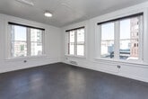 This single-floor urban unit blends classic architectural bones with modern finishes throughout. Multiple large, white-trimmed windows flood the living spaces with abundant natural light while offering views of the surrounding cityscape. The open layout creates a generous sense of space, with smooth concrete-style flooring flowing through the main living and kitchen areas.

The kitchen is well-appointed with white shaker-style cabinetry, granite countertops, and a full suite of stainless steel appliances, including a refrigerator, electric range, built-in microwave, and dishwasher — delivering both style and functionality.

The sleeping area features plush carpeting underfoot and a built-in wardrobe with sliding doors, offering ample storage with integrated shelving and drawers. A stacked washer and dryer unit is conveniently located nearby, adding in-unit laundry to the unit's practical amenities.

The bathroom is clean and contemporary, featuring a double-sink vanity with white cabinetry and marble-style countertops, a large mirror, and a glass-enclosed walk-in shower. A wall-mounted mini-split system provides efficient climate control throughout.

Exposed conduit along the ceilings adds an industrial character that complements the building's urban setting, giving the space a distinctive and modern edge.