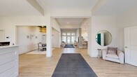 Located at 2335 N Cassady Ave in Columbus, Ohio, the Eden Park community clubhouse by Ardent Communities offers a thoughtfully designed, single-floor gathering space spanning a generous footprint. Guests are welcomed at a sleek white reception desk adorned with pendant lighting and branded signage, setting a polished, professional tone from the moment of entry. Light hardwood flooring flows throughout, tying together the various zones of the space with a clean, cohesive aesthetic. The open-concept layout connects multiple living and lounge areas, including a spacious great room featuring a pool table, comfortable seating arrangements, a fireplace, and a wall-mounted television. An accent wall in rich teal adds a bold design element to a secondary lounge, which opens via double doors for flexible use. Tall windows flood the interiors with abundant natural light and offer views of the surrounding neighborhood. The full kitchen is outfitted with stainless steel appliances, white shaker cabinetry, quartz countertops, and a breakfast bar with woven rattan barstools beneath elegant cone pendant lights. A separate dining nook with chandelier lighting provides a more intimate setting. The overall ambiance is bright, modern, and inviting, blending upscale finishes with comfortable, community-oriented design.