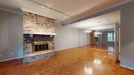 This two-floor home offers a thoughtful blend of classic character and functional design across its well-proportioned living spaces. The main living area immediately draws attention with its striking floor-to-ceiling brick fireplace with a brass-trimmed surround, complemented by warm parquet hardwood flooring that extends throughout the lower level. Track lighting runs along the ceiling, providing adjustable illumination, while a wall of floor-to-ceiling mirrors visually expands the space and reflects a classic chandelier overhead. Plantation shutters on the windows allow for controlled natural light throughout.

The kitchen is well-equipped, featuring white cabinetry, dark granite countertops, a tile backsplash, and stainless steel appliances including a dishwasher, range, and microwave. A pendant light fixture and a sliding glass door leading to an outdoor area add both style and functionality to this galley-style space.

A carpeted staircase with a wood handrail connects to the upper floor, where additional rooms feature hardwood flooring and crown molding. The upper-level bathroom is finished with a granite-topped vanity, modern tile flooring, and a tiled walk-in shower with a glass enclosure, offering a clean and updated aesthetic throughout.