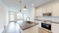 This single-floor residence offers a thoughtfully designed open-concept layout that seamlessly connects the kitchen and living room, creating a comfortable and functional living environment. Warm hardwood-style flooring runs consistently throughout the unit, tying each space together cohesively.

The kitchen serves as a central focal point, anchored by a large island with a dark quartz countertop, an integrated sink, and a brushed gold faucet. Pendant lights with brass fixtures hang above the island, complementing the white shaker cabinetry, white subway tile backsplash, and a full suite of stainless steel appliances, including a refrigerator, electric range, and microwave.

The living room benefits from an expansive bank of windows that frame outdoor greenery, filling the space with natural light and providing views of a landscaped courtyard. A ceiling fan is centrally positioned overhead.

The primary bedroom is generously sized, featuring crown molding, a ceiling fan, and windows with outdoor views. The second bedroom offers a clean, neutral palette with the same hardwood-style flooring. Three closets, including a walk-in with wire shelving, provide ample storage.

Both bathrooms are finished with dark countertops, white cabinetry, and tiled tub-shower combinations.