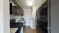 This single-floor residence offers a practical and comfortable layout designed to maximize everyday living. The galley-style kitchen is efficiently organized, featuring dark espresso cabinetry, granite-look countertops, hardwood-style flooring, and a full suite of black appliances including a gas range, microwave, dishwasher, and a large refrigerator. A stacked washer and dryer unit is conveniently tucked within the kitchen area, adding in-unit laundry without sacrificing much space.

The living area is generously sized, finished with neutral-toned carpet and light gray walls that create a calm, versatile backdrop. A sliding glass door opens directly to a private balcony, flooding the space with natural light and offering an outdoor retreat. The bedroom spaces are similarly appointed with plush carpet, large windows that invite natural light, and ample room for furnishings.

The bathroom features a tub-shower combination with white tile surround and classic, clean finishes throughout. The overall design of the residence is straightforward and functional, with a neutral color palette that provides a move-in-ready canvas adaptable to a variety of personal styles.