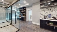 This single-floor commercial space in New Brunswick, NJ, is designed with a sleek, contemporary aesthetic that balances functionality and style. The layout centers around a striking glass-walled office suite enclosed by floor-to-ceiling glass panels with matte black framing, providing full visibility while maintaining a distinct sense of separation between work areas. Inside, ergonomic seating and dark wood desks are set atop light-toned carpeting, creating a professional environment well-suited for focused work or meetings.

The connecting corridor and common areas feature rich, wood-look tile flooring in warm gray tones, lending a cohesive flow throughout the space. Recessed lighting and coffered ceiling details add architectural depth, while neutral gray walls provide a refined, understated backdrop.

A dedicated lounge and refreshment area serves as a practical amenity hub, complete with built-in dark cabinetry, open shelving in a warm wood tone, a beverage machine, a under-counter refrigerator, and a geometric mosaic tile backsplash that introduces a decorative focal point. A built-in countertop with bar seating offers an additional casual workspace. Together, these elements create a polished, well-appointed environment ideal for a professional office setting.