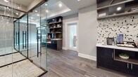 This single-floor commercial space in New Brunswick, NJ, is designed with a sleek, contemporary aesthetic that balances functionality and style. The layout centers around a striking glass-walled office suite enclosed by floor-to-ceiling glass panels with matte black framing, providing full visibility while maintaining a distinct sense of separation between work areas. Inside, ergonomic seating and dark wood desks are set atop light-toned carpeting, creating a professional environment well-suited for focused work or meetings.

The connecting corridor and common areas feature rich, wood-look tile flooring in warm gray tones, lending a cohesive flow throughout the space. Recessed lighting and coffered ceiling details add architectural depth, while neutral gray walls provide a refined, understated backdrop.

A dedicated lounge and refreshment area serves as a practical amenity hub, complete with built-in dark cabinetry, open shelving in a warm wood tone, a beverage machine, a under-counter refrigerator, and a geometric mosaic tile backsplash that introduces a decorative focal point. A built-in countertop with bar seating offers an additional casual workspace. Together, these elements create a polished, well-appointed environment ideal for a professional office setting.