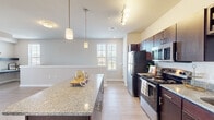 This single-story unit at Grand Overlook in Memphis, Tennessee offers a thoughtfully designed open-concept layout that seamlessly connects the kitchen, dining, and living areas. The kitchen serves as the centerpiece of the space, showcasing rich dark-espresso cabinetry, granite countertops, a large central island with pendant lighting overhead, and a full suite of stainless steel appliances including a refrigerator, range, microwave, and dishwasher. Track lighting and a wine rack built into the upper cabinetry add functional detail to the space.

Light wood-style flooring extends throughout the main living areas, complementing the neutral wall tones and creating a clean, cohesive aesthetic. The living area is generously proportioned, featuring a ceiling fan, multiple windows with blinds that invite natural light, and a glass door leading to an outdoor area. A built-in shelf adds a subtle architectural accent.

The bedroom features plush carpeting, a ceiling fan, and windows that bring in ample natural light. The full bathroom includes a tub/shower combination with built-in shelving and a crisp white surround. Throughout the unit, the design balances modern finishes with a comfortable, functional atmosphere.
