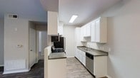This single-story space showcases a thoughtfully designed kitchen as its central feature. The kitchen is laid out in a galley-style configuration, maximizing functionality through an efficient use of space. White cabinetry lines the walls from counter height to ceiling, providing generous storage capacity. The upper cabinets are complemented by dark countertops, creating a clean contrast that adds visual interest to the space.

The kitchen is equipped with stainless steel appliances, including a dishwasher and refrigerator, alongside a gas range cooktop positioned at a peninsula that separates the kitchen from the adjoining area. A stainless steel sink is installed along the main counter run, accompanied by standard fixtures. Recessed and flush-mounted ceiling lighting ensures the workspace is well-illuminated throughout.

Wood-look flooring runs through the kitchen and into the adjacent space, offering a durable and cohesive aesthetic. The neutral color palette of white walls and cabinetry keeps the interior feeling bright and open. A doorway visible beyond the kitchen suggests additional rooms, indicating a connected and practical floor plan overall.