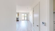 This well-designed single-floor unit offers a clean, contemporary aesthetic defined by crisp white walls, recessed lighting, and light-toned wood-style flooring that runs seamlessly throughout the entire space. The open-plan layout connects the living area to the kitchen, creating a bright and airy environment that makes excellent use of the available floor area.

The kitchen is a standout feature, outfitted with flat-front light wood cabinetry, a white subway tile backsplash, and a full suite of stainless steel appliances including a refrigerator, gas range, over-the-range microwave, and dishwasher. A window above the sink and a sliding glass door to a private balcony flood the kitchen and living area with natural light, while offering pleasant outdoor views.

The living area is generously proportioned, providing a versatile open canvas with recessed ceiling lights, a ceiling vent for climate control, and clean white walls. A dedicated in-unit laundry closet with a stacked washer and dryer adds everyday convenience.

The bathroom is finished in the same modern style, featuring light wood floating cabinetry, an under-mount sink, a large mirror, globe sconce lighting, and a glass-enclosed shower stall, all tied together by the continuous wood-style flooring for a cohesive look throughout the unit.