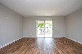This single-floor space offers an open and functional layout characterized by a clean, neutral aesthetic. The main living area showcases a combination of rich, dark hardwood flooring and plush carpeting, creating a natural visual distinction between zones within the space. The walls are finished in a warm beige tone, lending a welcoming and versatile backdrop that suits a variety of interior styles.

A track lighting fixture is mounted on the ceiling, providing adjustable, directional illumination across the room. The ceilings feature a subtle texture and are complemented by crisp white trim and baseboards throughout, adding a polished, finished look. A white paneled door leads to an adjacent area or hallway, partially revealing a connected space beyond.

Ventilation is provided via a ceiling-mounted HVAC vent, ensuring comfortable climate control. The open wall space offers ample flexibility for furniture arrangement. Overall, the space presents a practical and well-maintained interior with a straightforward, move-in-ready appeal suited for everyday living.