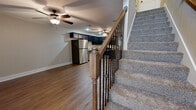 Located at 9540 N Main St in Kansas City, MO, this two-story home offers a well-organized layout spread across two floors. The main level hosts the combined kitchen and living area, as well as the attached garage. The living room features warm wood-look plank flooring, a ceiling fan, and a textured ceiling, creating a comfortable and functional gathering space. A staircase with a classic wooden newel post and decorative wrought-iron balusters connects the two floors seamlessly.

The kitchen is a standout feature, equipped with dark espresso cabinetry, light granite countertops, stainless steel appliances including a refrigerator, range, microwave, and dishwasher, along with a built-in wine rack for added character. The flooring continues the wood-look aesthetic throughout.

Upstairs, three bedrooms offer carpeted floors and neutral tones. The generously sized primary bedroom features vaulted ceilings, a ceiling fan, and direct access to an en-suite bathroom with a walk-in shower enclosed by glass doors. The second bathroom includes a tub-shower combination, a dark vanity, and wood-look flooring. The attached garage provides additional utility with an automatic opener.