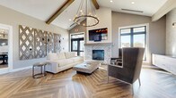 Located at 4328 Provision Parkway in Fort Wayne, Indiana, this single-story community clubhouse offers a thoughtfully designed gathering space with modern farmhouse aesthetics throughout. The main lounge serves as the heart of the facility, boasting soaring vaulted ceilings accented by exposed wood beams and a striking circular chandelier. A whitewashed brick fireplace with a mounted flat-screen TV anchors the room, while plush seating and herringbone-patterned hardwood flooring create a warm, inviting ambiance. Large windows flood the space with natural light and provide outdoor views. Adjacent to the lounge, the fully equipped kitchen features sleek dark wood cabinetry, quartz countertops, a decorative tile backsplash, and stainless steel appliances including a dishwasher, refrigerator, and wall oven — ideal for community events and gatherings. Multiple dining areas with round tables, modern black chairs, and contemporary chandeliers offer flexible seating arrangements. The fitness center is comprehensively outfitted with treadmills, ellipticals, cable machines, free weights, and cardio bikes, all set on durable hardwood-style flooring with large windows providing ample natural light. Together, these amenities create a polished and functional community hub.