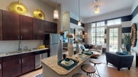 This thoughtfully designed single-floor residence blends modern aesthetics with comfortable living. The open-concept kitchen is a standout feature, boasting rich dark cabinetry that extends to impressive heights, granite countertops, stainless steel appliances including a refrigerator, range, microwave, and dishwasher, a white tile backsplash, and a central island with bar seating — all illuminated by striking gold disc pendant lights and soaring ceilings that amplify the sense of space.

The living area flows seamlessly from the kitchen and features bold navy and white horizontal striped accent walls, rich hardwood-style flooring, and large grid-paned windows and a glass French door that flood the space with natural light and offer outdoor views.

The bedroom is a serene retreat finished in calming teal tones, complete with large windows framing lush outdoor scenery, and is complemented by a spacious walk-in closet with built-in shelving and hardwood flooring. The en-suite bathroom features granite-topped dark wood cabinetry, large-format tile flooring, and a glass-enclosed shower.

A dedicated home office provides a focused workspace with generous natural light, built-in shelving, and vibrant artwork, rounding out this well-appointed and design-forward residence.