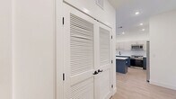 This well-appointed 2-bedroom, 2-bathroom residence at 555 Northfield Avenue in West Orange, NJ offers a thoughtfully designed single-floor layout with generous living space. The open-concept kitchen and living area is a standout feature, showcasing a striking two-tone design with navy blue lower cabinetry, white upper cabinets, a large waterfall-edge island, white quartz countertops, and stainless steel appliances — all complemented by light hardwood flooring and recessed lighting throughout. The living area extends to a private balcony through sliding glass doors, offering pleasant outdoor views. The spacious primary bedroom includes a walk-in closet with built-in shelving and rod systems, while the en-suite bathroom features elegant marble-style tile flooring, a floating dual-vanity with gray cabinetry, gold hardware accents, white quartz countertops, and a round gold-framed mirror. The second bedroom is bright and well-sized, with a large window framing natural light and outdoor treetop views. The second bathroom mirrors the same refined design aesthetic. Additional highlights include a den, dedicated laundry room, utility room, and an impressive six closets providing abundant storage throughout.