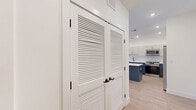 This well-appointed 2-bedroom, 2-bathroom residence at 555 Northfield Avenue in West Orange, NJ offers a thoughtfully designed single-floor layout with generous living space. The open-concept kitchen and living area is a standout feature, showcasing a striking two-tone design with navy blue lower cabinetry, white upper cabinets, a large waterfall-edge island, white quartz countertops, and stainless steel appliances — all complemented by light hardwood flooring and recessed lighting throughout. The living area extends to a private balcony through sliding glass doors, offering pleasant outdoor views. The spacious primary bedroom includes a walk-in closet with built-in shelving and rod systems, while the en-suite bathroom features elegant marble-style tile flooring, a floating dual-vanity with gray cabinetry, gold hardware accents, white quartz countertops, and a round gold-framed mirror. The second bedroom is bright and well-sized, with a large window framing natural light and outdoor treetop views. The second bathroom mirrors the same refined design aesthetic. Additional highlights include a den, dedicated laundry room, utility room, and an impressive six closets providing abundant storage throughout.