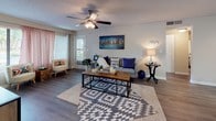 This single-floor residence offers a thoughtfully organized layout with interconnected living spaces designed for everyday comfort. The living room serves as the heart of the home, featuring wood-style flooring, a ceiling fan with light fixture, and a front entry door flanked by windows that allow natural light to fill the space. The room offers ample space for comfortable seating arrangements.

Adjacent to the living area, a compact dining nook accommodates an intimate table and seating, while the kitchen is equipped with white cabinetry, light wood-style flooring, and black appliances including a full-size refrigerator and electric range with overhead ventilation.

Both bedrooms are carpeted and each features a ceiling fan, a reach-in closet with bifold doors, and neutral wall tones. One bedroom includes a sliding glass door providing direct access to an outdoor area with exterior views, adding a notable sense of openness to the space.

The bathroom includes a single-sink vanity with white cabinetry, a large wall mirror, and a shower-tub combination with a curtain. Wood-style flooring continues throughout this space.

A dedicated laundry area houses a full-size side-by-side washer and dryer, with overhead shelving for additional storage. The overall design is consistent and functional throughout.