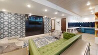 Located at 595 King St in the heart of Charleston, South Carolina, this thoughtfully designed single-floor community lounge space combines contemporary style with eclectic Southern charm. The open layout flows seamlessly from one zone to the next, united by warm wood-paneled ceilings, recessed lighting, and large-format tile flooring throughout.

The main lounge area anchors the space with a tufted green leather sofa set atop a blue-and-white patterned area rug, complemented by neutral accent chairs. A wall-mounted flat-screen television sits against a striking geometric black-and-white accent wall, creating a bold focal point. Large folding glass doors open directly to an outdoor pool area, flooding the space with natural light and providing a seamless indoor-outdoor connection.

Adjacent to the lounge, a dining nook features deep navy blue upholstered banquette seating with built-in display shelving above, paired with marble-topped tables and gold-framed acrylic chairs — an elegant yet inviting setup ideal for gathering or casual work sessions.

The bar area rounds out the space, showcasing a marble countertop with barstool seating, a beverage refrigerator, and a dramatic navy hexagonal tile backsplash. Together, these distinct zones create a versatile, design-forward communal space well-suited for socializing, dining, and relaxation.