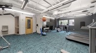 This well-appointed fitness center at 3924 Excelsior Blvd in St. Louis Park, Minnesota offers a comprehensive exercise facility designed to support a wide range of workout routines. The space is spread across a single floor and is characterized by its open, airy layout with notable ceiling height, exposed ductwork, and bright linear lighting that gives the room a clean, modern industrial aesthetic.

The flooring throughout is a distinctive teal-patterned carpet tile, adding a pop of color to the otherwise neutral gray and white palette of the walls and ceiling. Natural light filters in through multiple windows along the perimeter, providing views of the surrounding neighborhood and keeping the space feeling fresh and energized.

The cardio zone is well-equipped with multiple treadmills, an elliptical trainer, and a recumbent stationary bike, each featuring individual media screens for an engaging workout experience. A dedicated strength and functional training area includes a cable machine, a full dumbbell rack, stability balls, a BOSU trainer, step platforms, and a medicine ball, catering to a variety of fitness levels and training styles. A large wall-mounted mirror enhances the sense of space while allowing users to monitor their form. The facility is thoughtfully organized, spacious, and fully equipped to serve as a primary fitness destination.