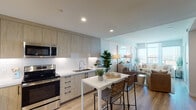 Located in the heart of downtown San Diego, this single-floor residence at 1150 E St offers a thoughtfully designed open-concept layout with modern finishes and sweeping city views. The kitchen is a standout feature, outfitted with light wood flat-panel cabinetry extending to the ceiling, white subway tile backsplash, quartz countertops, and a full suite of stainless steel appliances including a French door refrigerator, electric range, built-in microwave, and dishwasher. A compact movable island with bar seating provides a casual dining option and flows naturally into the living area. The living room is bathed in natural light from floor-to-ceiling windows, framing panoramic views of the San Diego skyline. Light hardwood flooring runs continuously throughout the main living spaces, enhancing the airy and cohesive feel of the home. The bedroom features the same expansive city views through large corner windows, a mirrored sliding-door closet, and direct access to the rest of the unit. The bathroom is finished with a warm wood vanity, grey quartz countertop, undermount sink, a mirrored medicine cabinet, and a tiled walk-in shower. Clean lines, recessed lighting, and a neutral color palette contribute to the overall contemporary and functional ambiance of this well-appointed downtown residence.