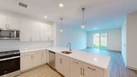 This thoughtfully designed single-story home offers three bedrooms and two bathrooms across a well-utilized floor plan. The open-concept kitchen and living area serves as the heart of the home, featuring crisp white cabinetry, a large peninsula with a stainless steel sink, white quartz countertops, and a subway tile backsplash. Stainless steel appliances — including a refrigerator with ice maker, range, and microwave — complete the kitchen. Stylish globe pendant lights hang above the peninsula, adding a modern touch. Light wood-style flooring flows consistently throughout the main living areas and bedrooms, creating a cohesive and contemporary aesthetic. The living area opens directly to the backyard through a sliding glass door, allowing abundant natural light and seamless indoor-outdoor connectivity. The backyard is generously sized, enclosed by a wood privacy fence, and features a lush green lawn. The bedrooms are bright and neutrally finished, with windows offering views of the surrounding greenery. The primary bathroom includes a sleek walk-in shower with a sliding glass door and a vanity with white countertops, while the second bathroom offers a full tub-shower combination. Clean white walls and recessed lighting throughout contribute to the home's light, airy, and move-in-ready appeal.