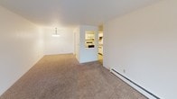 This single-floor residence presents a straightforward and functional layout designed for comfortable everyday living. The living area is generously sized, featuring neutral-toned wall-to-wall carpeting, a textured ceiling, and a sliding glass door that opens to a balcony, allowing natural light to fill the space. A wall-mounted air conditioning unit provides climate control. Adjacent to the living area, a dedicated dining space is highlighted by a pendant chandelier, with an open pass-through connecting to the kitchen for a sense of openness.

The kitchen is well-appointed with ample white cabinetry trimmed in warm wood tones, a double-basin stainless steel sink, laminate countertops, and a white dishwasher. Tile-style flooring adds a practical touch in this area. The bedrooms are carpeted and bright, with one featuring a sliding window that brings in natural light, complemented by baseboard heating.

The bathrooms offer clean, utilitarian fixtures — one includes a full soaking tub with a shower combination and chrome hardware, while the other features a standalone shower stall. Warm wood-trimmed doors and neutral walls throughout give the space a cohesive, understated aesthetic.
