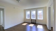Located along City Avenue in Philadelphia, PA, this single-floor unit offers a clean and classic living environment with thoughtful architectural details throughout. The main living area is a standout feature, showcasing rich, dark hardwood floors that add warmth and character to the space. A bank of three large windows lines one wall, allowing an abundance of natural light to pour in and illuminate the room, with views of the surrounding neighborhood. A traditional cast-iron radiator sits beneath the windows, a nod to the building's classic construction and providing efficient heating. The walls are finished in a soft, neutral tone that complements the natural light and enhances the open, airy feel of the room. Crown molding and clean white baseboards frame the space with refined architectural detail. The ceiling is smooth and well-proportioned, contributing to the room's balanced and comfortable scale. Overall, the unit reflects a well-maintained, timeless aesthetic that combines functional living with enduring design elements, making it a welcoming and practical space in a well-established Philadelphia corridor.
