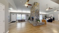 Located at 2505 5th Street in Davis, California, this single-story clubhouse offers a well-rounded community facility spanning a generous footprint across one floor. The centerpiece of the space is a soaring, floor-to-ceiling river-rock fireplace that anchors the main lounge area, rising dramatically beneath vaulted ceilings fitted with ceiling fans. Light wood-tone flooring runs throughout, lending warmth and visual continuity across the open layout. Large windows and sliding glass doors flood the lounge and dining area with abundant natural light, while providing views of the surrounding outdoors. The lounge comfortably accommodates seating arrangements alongside a dining table, making it suitable for both casual gatherings and organized events. A dedicated business room features a long central conference table, built-in desk workstations along the walls, computer terminals, and vaulted ceilings — ideal for meetings, study sessions, or remote work. The fitness center is well-appointed with cardio equipment including treadmills and an elliptical, a dumbbell rack, a weight bench, and floor-to-ceiling mirrors that enhance the sense of space. Motivational signage and rubber flooring complete the workout environment. Together, these distinct areas make this clubhouse a functional and inviting hub for community life.
