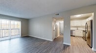 This single-story unit combines practical design with clean, modern finishes throughout. The open living area is anchored by durable gray-tone luxury vinyl plank flooring and neutral gray walls, creating a cohesive, contemporary aesthetic. A ceiling fan overhead and a large sliding glass door with vertical blinds allow for ample natural light and comfortable airflow, while textured ceilings add a traditional touch.

The kitchen is efficiently laid out with crisp white shaker-style cabinetry extending to the ceiling for generous storage, white countertops, and a full suite of stainless steel appliances including an electric range, built-in microwave, dishwasher, and refrigerator. Light-toned LVP flooring ties the kitchen seamlessly to the main living space.

A hallway connects the living area to the bedrooms, each finished with plush, neutral-toned carpet and soft gray walls. The bedrooms offer good proportions, natural light from windows with blinds, and closet storage. One bedroom features direct access to a bathroom, providing added privacy. The bathroom area includes white cabinetry with gold-toned hardware and matching LVP flooring, maintaining the consistent, updated style found throughout the unit.