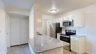 Located at 5959 Cougar Ln in Kearns, Utah, this well-appointed one-bedroom, one-bathroom residence offers a thoughtfully designed single-floor layout with a clean, modern aesthetic throughout. The open-concept living, dining, and kitchen area serves as the heart of the home, featuring light wood-style flooring, crisp white walls, and a stylish chandelier that anchors the dining space. The kitchen is outfitted with white shaker-style cabinetry, granite countertops with a peninsula overhang, a subway tile backsplash, a stainless steel sink, and a full suite of stainless steel appliances including a refrigerator, electric range, microwave, and dishwasher. The bedroom is a comfortable, carpeted retreat with a natural light source from a window fitted with blinds, offering a calm and private atmosphere. The bathroom includes a granite-topped vanity with an undermount sink, a full tub and shower combination, and wood-style flooring for a cohesive finish. The unit also features a private balcony, a utility room, two hallways, and an impressive four closets providing generous storage throughout. The overall ambiance is bright, clean, and move-in ready, making this a highly functional and welcoming space.