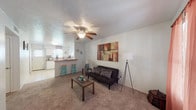 This single-story home offers a practical and comfortable layout with well-defined living spaces. The living room serves as the central gathering area, featuring carpet flooring, a ceiling fan with light fixture, and a textured ceiling. It connects seamlessly to the kitchen via a breakfast bar with seating, creating an open, sociable flow between the two spaces.

The kitchen is well-equipped with white cabinetry featuring wood-trimmed accents, granite-style countertops, a double-basin sink, a dishwasher, and a range. Tile flooring and multiple windows allow natural light to brighten the workspace, while a back door provides direct exterior access.

The home includes multiple carpeted bedrooms, each with ceiling fans, windows dressed with patterned curtains, and ample wall space. One additional room functions effectively as a home office or flexible living space, also carpeted and outfitted with a ceiling fan and a window.

The bathroom features tile flooring, a granite-style vanity countertop, a toilet, and a shower-tub combination enclosed with sliding glass doors. A window above the tub area allows natural light to filter in, contributing to a bright and clean atmosphere throughout the home.