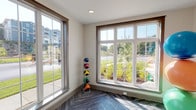 Located at 898–906 Emory Church Rd in Knoxville, Tennessee, this single-floor fitness facility is designed to provide a welcoming and fully equipped environment for exercise and wellness. The space is defined by an abundance of natural light, courtesy of multiple large, grid-pane windows framed in warm wood tones that offer views of the surrounding landscaped grounds and neighboring community. The distinctive herringbone-patterned flooring in a deep charcoal finish runs throughout, lending a polished, contemporary aesthetic to the interior. Neutral warm-white walls and recessed lighting contribute to a clean, open atmosphere. The main exercise area is generously proportioned and accommodates a variety of workout equipment, including a rack of color-coded medicine balls and a collection of stability balls in vibrant hues. A dedicated cycling zone features stationary spin bikes positioned beneath a wall-mounted flat-screen display, ideal for guided or independent cardio sessions. The space is accessed through a glass-paned interior door, adding a refined architectural detail while maintaining visual connectivity between areas. Overall, this fitness space strikes a balance between functional design and an inviting ambiance, making it a well-appointed amenity for active residents in the Knoxville area.
