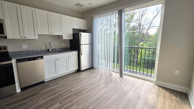 Kitchen and living area with balcony of an available apartment unit at Greenwood Commons Apartments in Delaware, OH. - Greenwood Commons Apartments