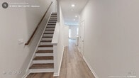 Located at 440 Hawthorne View Ct in Fuquay-Varina, NC, this well-appointed home presents a clean, modern aesthetic throughout. Light-toned luxury vinyl plank flooring flows seamlessly across the main living areas, complemented by crisp white walls and recessed lighting that create a bright, welcoming atmosphere.

The kitchen serves as a focal point of the home, showcasing white shaker cabinetry with brushed nickel hardware, quartz countertops with subtle veining, and a full suite of stainless steel appliances including a range, microwave, and refrigerator. A central island with a sink adds both functionality and a natural gathering space that opens to the adjacent living area. The living room is generously sized, featuring access to the outdoors through a rear door and windows that bring in natural light.

The bedrooms offer comfortable proportions with large windows fitted with blinds providing outdoor views and privacy. One bedroom connects directly to a well-designed en-suite bathroom featuring a double-sink vanity with white cabinetry, quartz countertops, tile flooring, a glass-enclosed walk-in shower, and accent lighting. A staircase with wood-toned treads and a warm handrail suggests additional levels for expanded living. The overall design reflects a thoughtfully executed, move-in-ready home with consistent, contemporary finishes throughout.