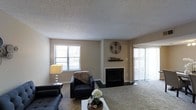 This two-floor residence offers a comfortable and functional layout designed for everyday living. The main living area serves as the heart of the home, centered around a classic fireplace with a dark surround and a decorative mantel, creating a warm and inviting focal point. Plush wall-to-wall carpeting adds a cozy feel underfoot, while neutral-toned walls provide a versatile backdrop for a variety of interior styles. Natural light flows generously into the space through a large window and a sliding glass door fitted with vertical blinds, offering both brightness and privacy. The textured popcorn ceiling adds a layer of dimension to the room's overall aesthetic. The living space is well-proportioned, accommodating a seating arrangement with ease while maintaining an open, uncluttered feel. The layout across two floors suggests a thoughtful separation of living and private spaces, lending the home a sense of organization and flow. Overall, the space presents a straightforward, livable design with classic residential features that offer a solid foundation for personalization and comfort.