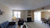 This two-floor residence offers a comfortable and functional layout designed for everyday living. The main living area serves as the heart of the home, centered around a classic fireplace with a dark surround and a decorative mantel, creating a warm and inviting focal point. Plush wall-to-wall carpeting adds a cozy feel underfoot, while neutral-toned walls provide a versatile backdrop for a variety of interior styles. Natural light flows generously into the space through a large window and a sliding glass door fitted with vertical blinds, offering both brightness and privacy. The textured popcorn ceiling adds a layer of dimension to the room's overall aesthetic. The living space is well-proportioned, accommodating a seating arrangement with ease while maintaining an open, uncluttered feel. The layout across two floors suggests a thoughtful separation of living and private spaces, lending the home a sense of organization and flow. Overall, the space presents a straightforward, livable design with classic residential features that offer a solid foundation for personalization and comfort.