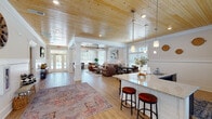 Located on Dunhagan Road in Greenville, North Carolina, this single-story clubhouse offers a well-appointed community gathering space defined by warm architectural details and an open, airy layout. The great room serves as the heart of the building, showcasing striking tongue-and-groove wood plank ceilings that soar overhead, recessed lighting, and elegant ceiling fans. Decorative white columns with paneled bases frame the open floor plan, complementing the white wainscoting and chair-rail millwork that lines the walls throughout. Light hardwood flooring flows seamlessly across the main area, enhancing the bright, welcoming atmosphere.

The lounge area is generously proportioned, accommodating comfortable leather seating arranged around a rustic wood coffee table. Adjacent dining areas feature round tables positioned beside large windows fitted with plantation-style blinds, offering views of an outdoor pool deck. French doors provide direct access to the exterior, flooding the interior with natural light.

The kitchenette is equipped with dark cabinetry, granite countertops, stainless steel appliances including a refrigerator and microwave, and a peninsula with bar seating. A dedicated fitness center rounds out the space, outfitted with treadmills, a stationary bike, an elliptical, free weights, and a wall-mounted television, with windows overlooking the surrounding landscape.