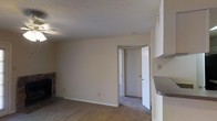 This single-floor space features a straightforward and functional layout with neutral design elements throughout. The main living area is finished with wall-to-wall carpeting in a warm beige tone, contributing to a comfortable, understated atmosphere. Smooth, neutral-painted walls are complemented by white baseboards, maintaining a clean and cohesive aesthetic.

A notable feature of the living area is the fireplace with a dark stone surround visible along one wall, providing a focal point and adding a cozy element to the space. The textured popcorn ceiling adds a classic touch consistent with the overall character of the unit.

A doorway from the living area leads into an adjacent room or hallway, suggesting an accessible and connected floor plan. A partial view of what appears to be a countertop or ledge is visible along the right edge, hinting at a nearby kitchen or utility area.

Overall, the space presents a clean, move-in-ready environment with practical finishes, offering a neutral canvas that is easy to personalize. The single-floor layout ensures convenient accessibility throughout.