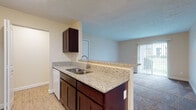 Located at 2389 Bayside Dr in Columbus, Ohio, this single-story unit presents a practical and cohesive layout with consistent finishes throughout. The open-concept living and dining area is finished with wall-to-wall carpet and neutral beige walls, creating a warm, inviting atmosphere. A sliding glass door fitted with vertical blinds allows natural light to fill the space while providing outdoor views and exterior access.

The kitchen is positioned adjacent to the main living area and features rich, dark-toned cabinetry paired with granite-style countertops and a peninsula with a stainless steel sink, offering both workspace and a casual breakfast bar. Wood-look flooring runs through the kitchen, adding a clean contrast to the carpeted areas. White appliances, including a range and refrigerator, complete the functional setup, with additional upper cabinetry providing storage.

The bedrooms are carpeted and finished with the same neutral palette, each featuring windows with blinds that bring in natural light and outdoor views. The bathroom is well-appointed with a dark wood vanity, granite countertop, a framed mirror, and a full tub-shower combination, all set on wood-look flooring. The overall design is clean, cohesive, and move-in ready.