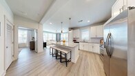 Located in Kennesaw, GA, this well-appointed 2-bedroom, 2-bathroom single-floor residence offers a functional and stylish layout designed for comfortable everyday living. The open-concept kitchen and living area serves as the heart of the home, anchored by a large granite-topped island with seating, white shaker cabinetry, a subway tile backsplash, stainless steel appliances, and pendant lighting. Light wood-tone flooring flows throughout, lending warmth and visual continuity across all spaces. The living room is generously sized, featuring multiple large windows with floor-to-ceiling drapes that invite abundant natural light and offer views of the surrounding greenery. The spacious primary bedroom includes a ceiling fan, easy access to the en suite bathroom, and connects to a walk-in closet outfitted with wire shelving systems for ample storage. The primary bathroom features a double vanity with granite countertops, a glass-enclosed walk-in shower with white subway tile, and light wood flooring. The second bedroom also benefits from natural light through a large window. The second bathroom includes a granite vanity and a tiled tub-shower combination. A hallway connects the private spaces efficiently, completing a cohesive and well-planned floor plan.